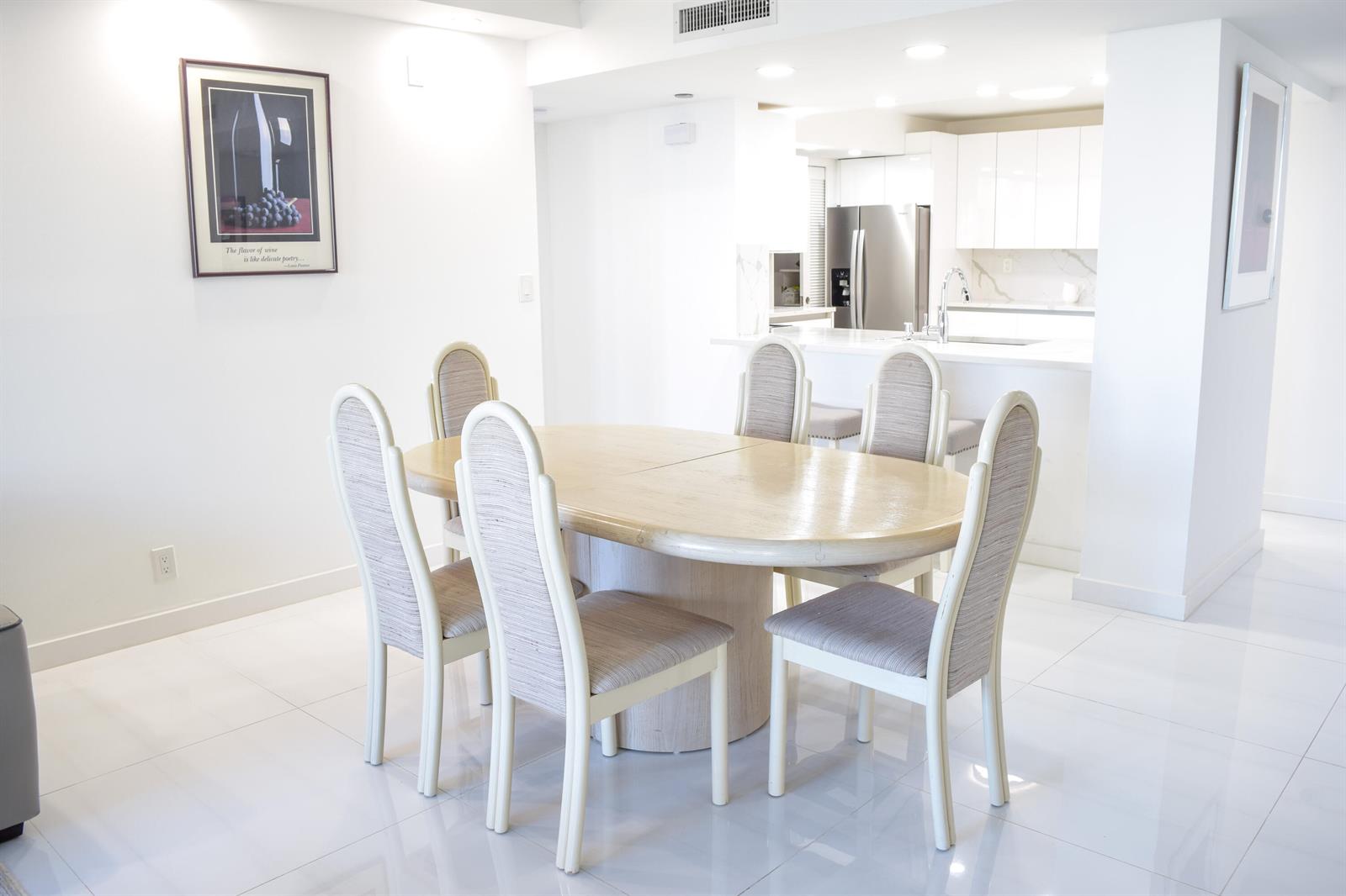 A dining area with a light wood table and six chairs sits before a white kitchen — 3420 S Ocean Boulevard # 7o, Highland Beach FL 33487, HIGHLAND BEACH, FL