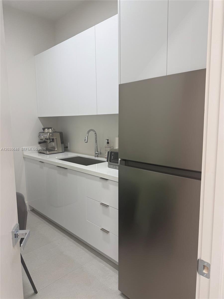 This kitchen features white flat-panel cabinetry, a stainless steel refrigerator, and a small sink — SWEETWATER, FL