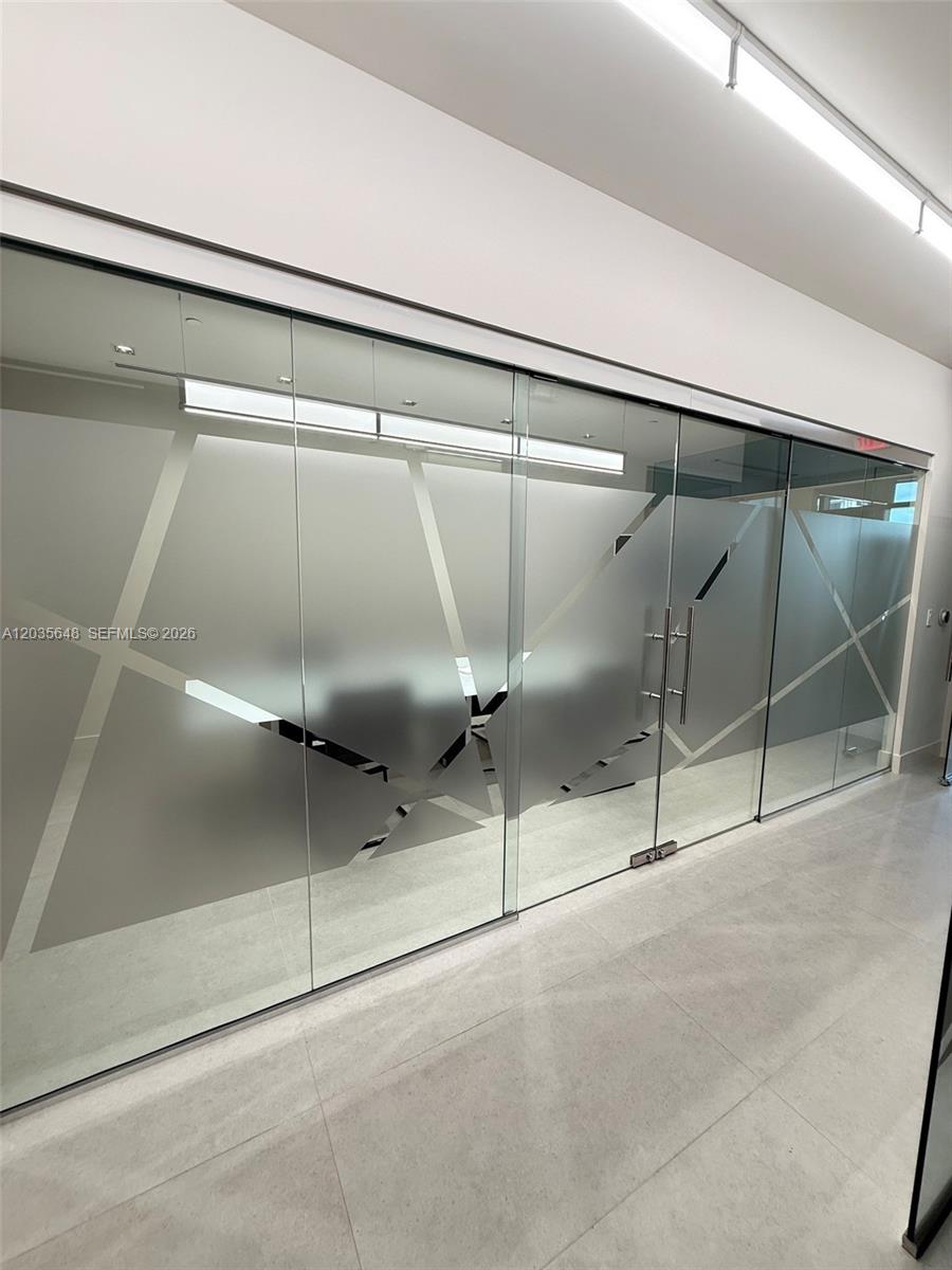 A glass-walled office partition features geometric frosted patterns and metal door handles — SWEETWATER, FL