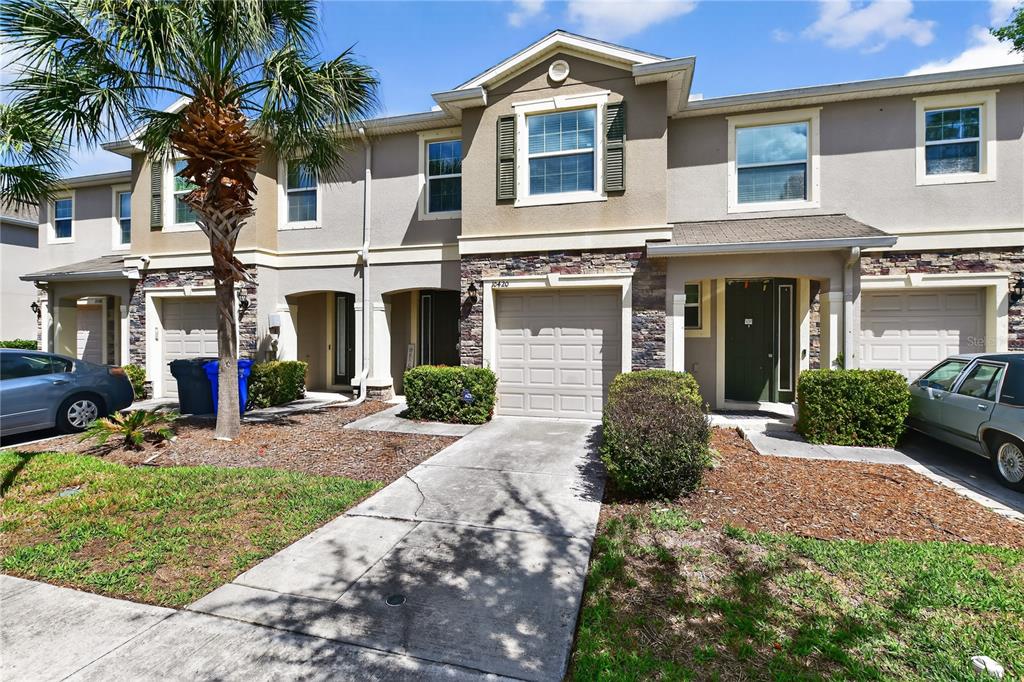A row of two-story townhomes with beige stucco facades, stone accents, and attached garages — 10420 BUTTERFLY WING COURT, RIVERVIEW, FL