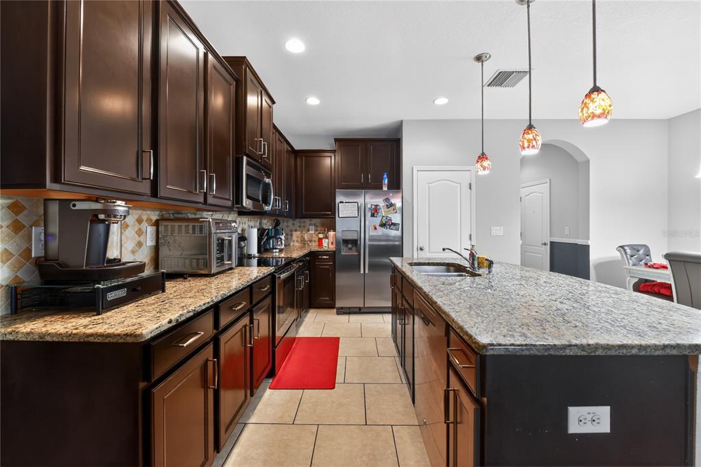 A kitchen features dark wood cabinets, granite countertops, a center island, and stainless steel appliances — 10420 BUTTERFLY WING COURT, RIVERVIEW, FL
