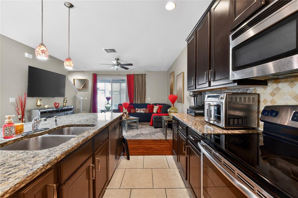 A kitchen with granite countertops and dark wood cabinets overlooks a living room area — 10420 BUTTERFLY WING COURT, RIVERVIEW, FL
