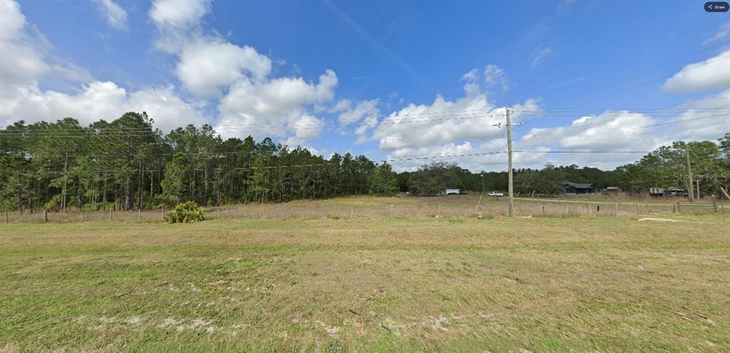 A wide, grassy, undeveloped lot features a wire fence and a line of pine trees — COMMONWEALTH AVE N, POLK CITY, FL