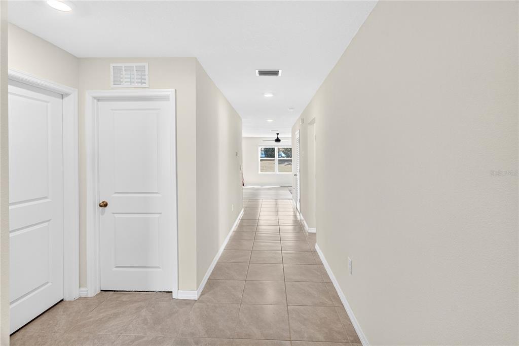 A hallway with light-colored walls and tiled flooring leads toward a bright living area — 17499 NW 172ND AVENUE, ALACHUA, FL