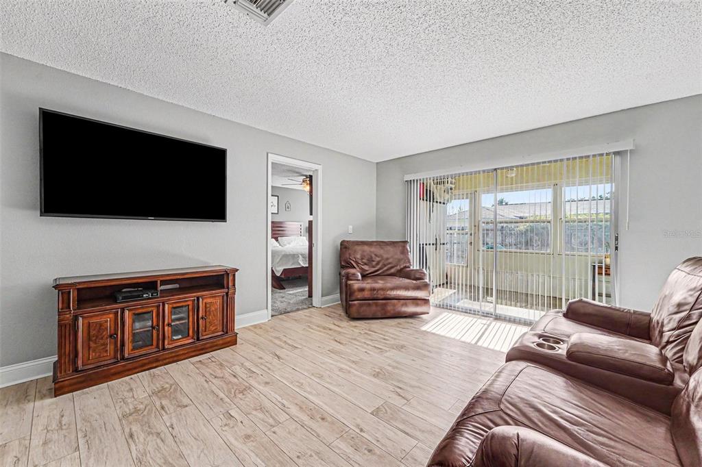 A living room features light wood-look tile flooring, a wall-mounted television, and brown leather furniture — 3402 TEESIDE DRIVE, NEW PORT RICHEY, FL