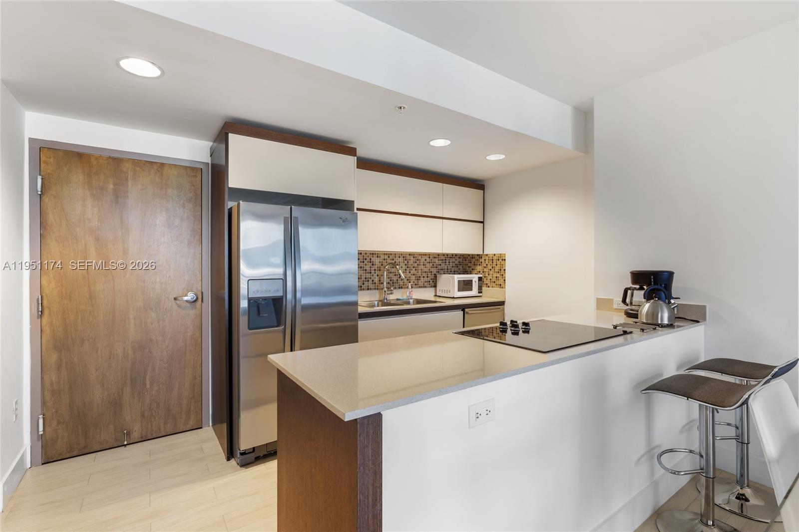 A modern open-concept living and dining area features a kitchen island, glass table, and sofa — 2155 Washington Ct # 401, Miami Beach FL 33139, MIAMI BEACH, FL