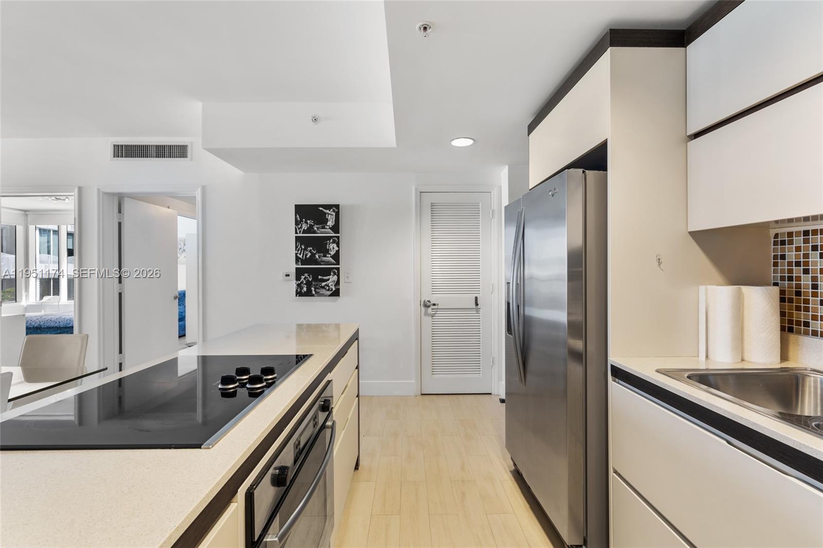 A modern kitchen features stainless steel appliances, white cabinetry, and a breakfast bar with stools — 2155 Washington Ct # 401, Miami Beach FL 33139, MIAMI BEACH, FL