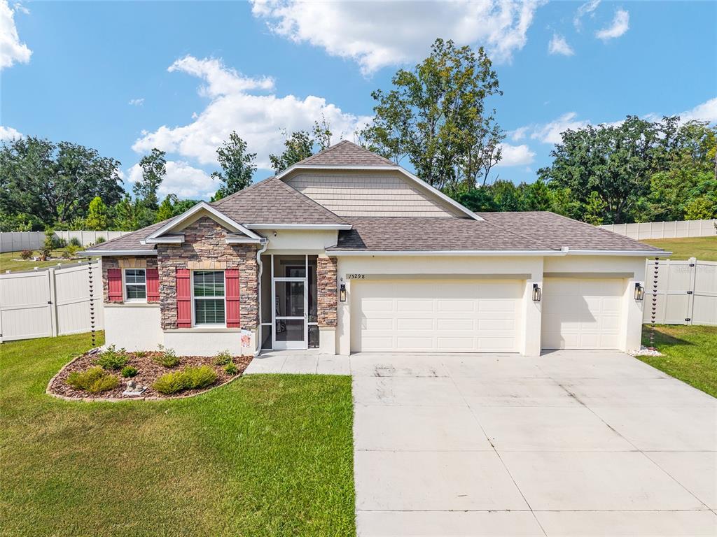 A single-story suburban house with a stone facade, red shutters, and a three-car garage — 15298 NW 121ST PLACE, ALACHUA, FL