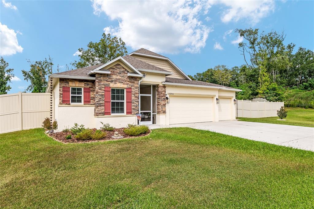 A single-story house with a stone facade, red shutters, and a three-car garage — 15298 NW 121ST PLACE, ALACHUA, FL