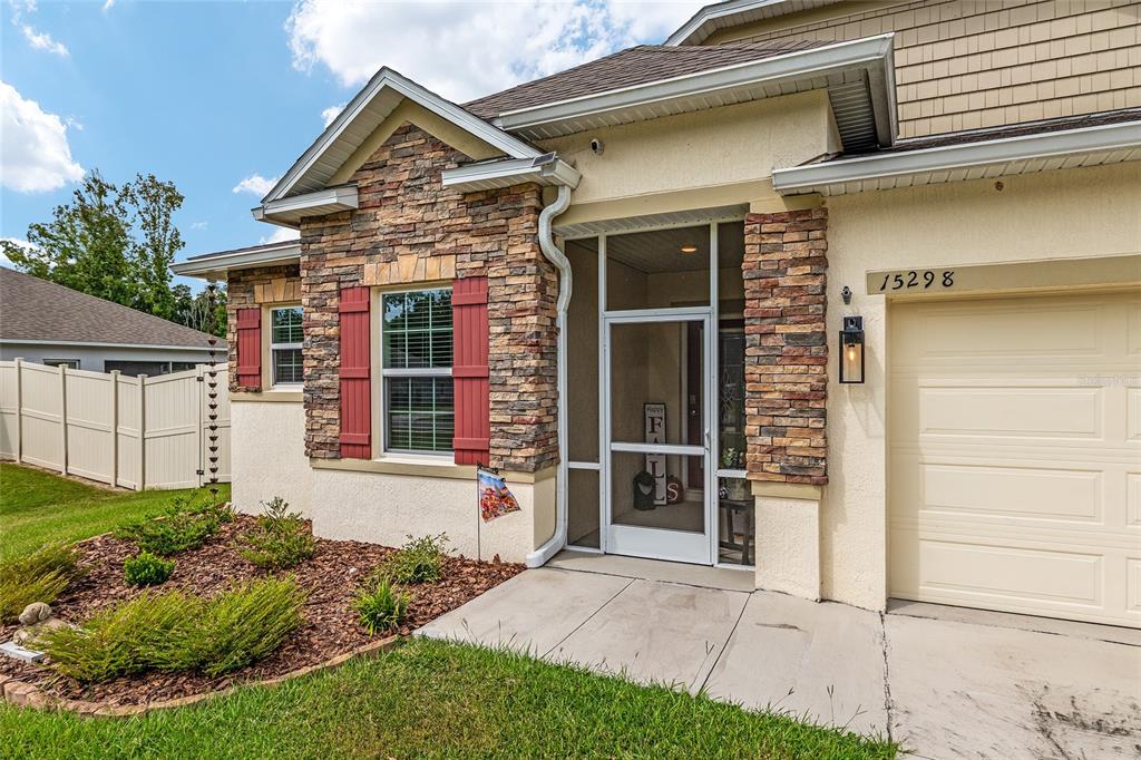 The exterior of a house features stone veneer, red shutters, and a screened-in front entryway — 15298 NW 121ST PLACE, ALACHUA, FL