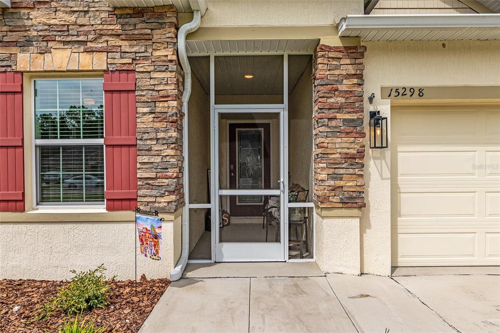 A house exterior features a stone-accented facade, a screen door, and a garage — 15298 NW 121ST PLACE, ALACHUA, FL