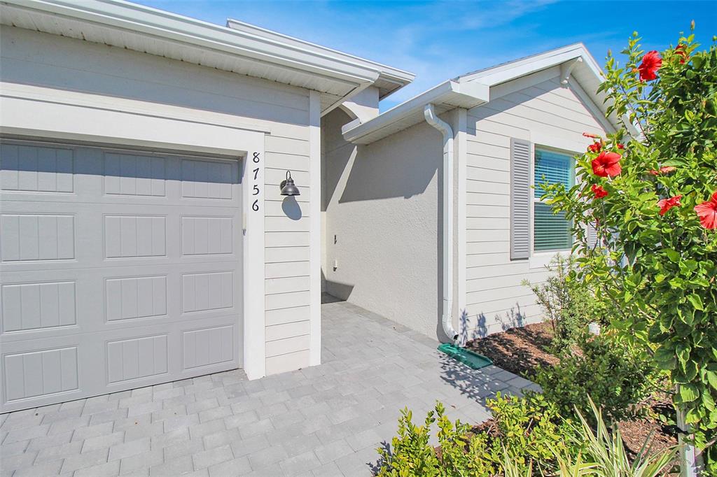 The exterior of a house features a gray garage door, light siding, and a paver walkway — 8756 COCO BAY BOULEVARD, ENGLEWOOD, FL