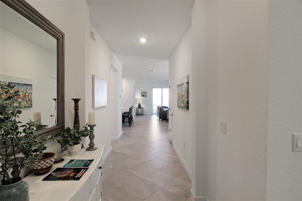 A tiled hallway leads from a foyer with a mirror toward a bright living area — 8756 COCO BAY BOULEVARD, ENGLEWOOD, FL