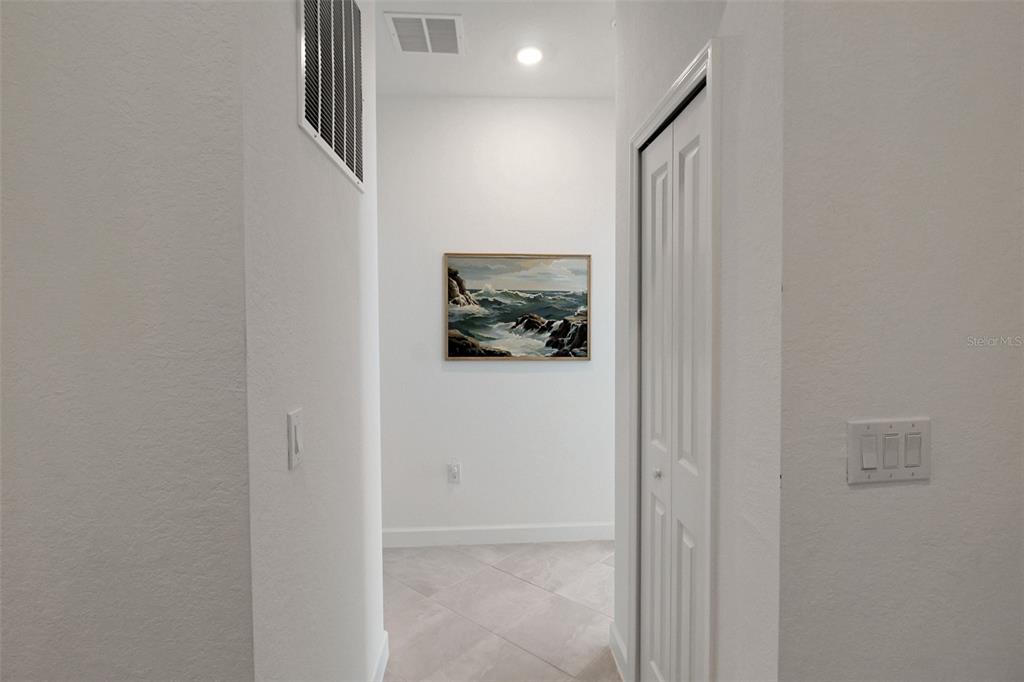 A hallway features white walls, tile flooring, a framed seascape painting, and a closet door — 8756 COCO BAY BOULEVARD, ENGLEWOOD, FL