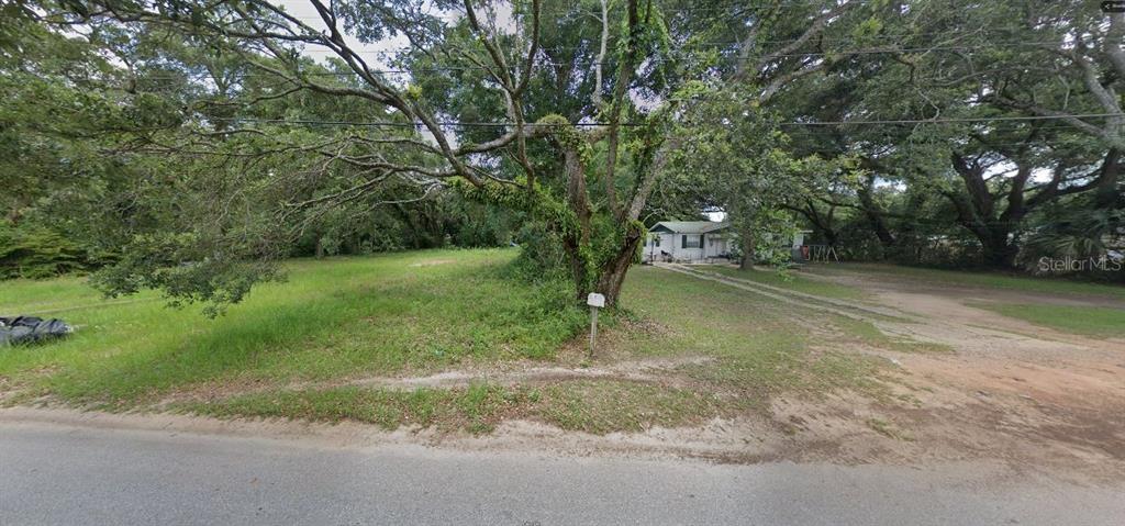 A large, grassy vacant lot with mature trees sits next to a small white house — 4203 N P STREET, PENSACOLA, FL