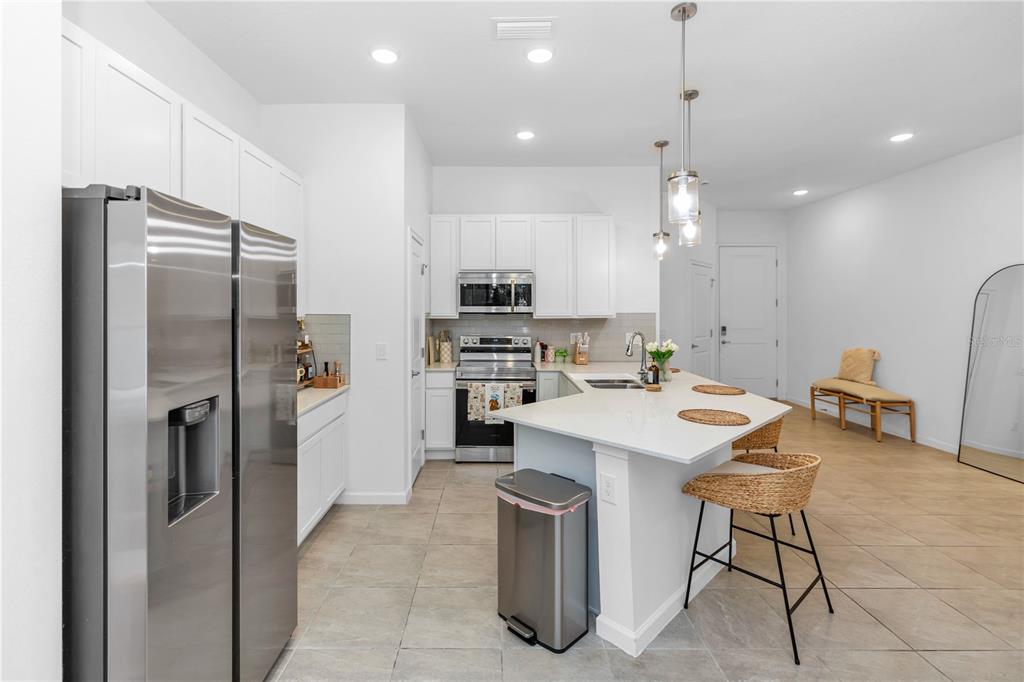 A modern kitchen features white cabinets, stainless steel appliances, a quartz island, and tile flooring — 10340 EBB TIDE LANE, ORLANDO, FL