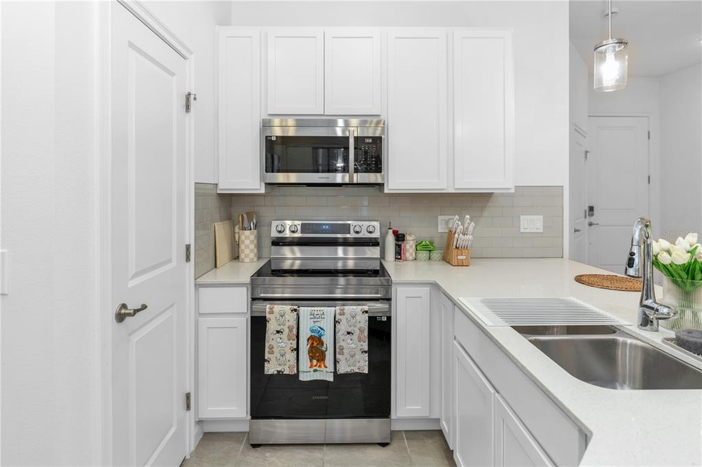 A kitchen features white cabinets, stainless steel appliances, a subway tile backsplash, and quartz countertops — 10340 EBB TIDE LANE, ORLANDO, FL