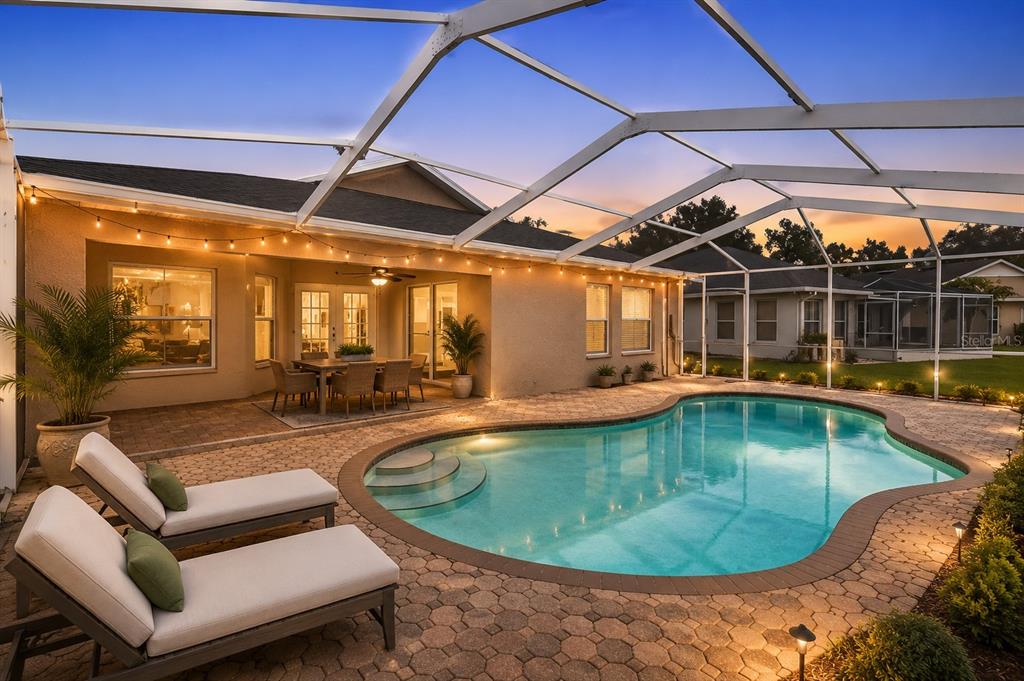 A screened-in patio features a swimming pool, lounge chairs, and a dining area at dusk — 19519 MORDEN BLUSH DRIVE, LUTZ, FL