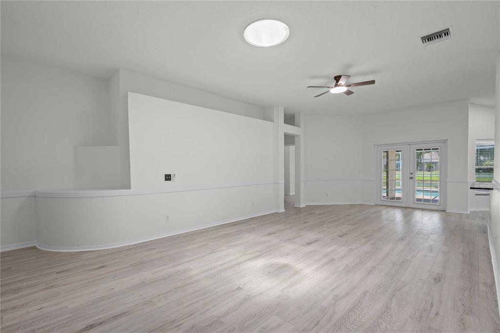 A bright living room features light wood-look flooring, a ceiling fan, and glass patio doors — 19519 MORDEN BLUSH DRIVE, LUTZ, FL