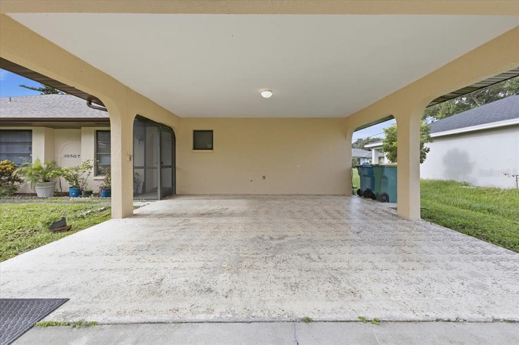 A covered concrete carport features arched support pillars and a screen door entrance — 10507 PENDLETON AVENUE UNIT B, ENGLEWOOD, FL