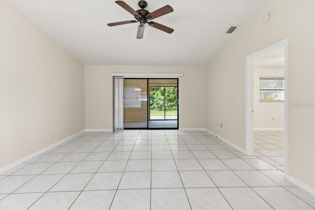 A living room with light-colored tile flooring, a ceiling fan, and sliding glass patio doors — 10507 PENDLETON AVENUE UNIT B, ENGLEWOOD, FL