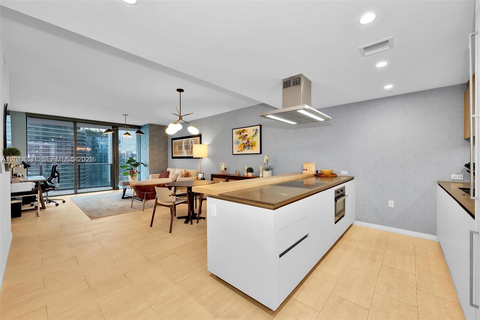 A modern open-concept kitchen and living area features a white island and light wood flooring — 1000 Brickell Plz # 3914, Miami FL 33131, MIAMI, FL