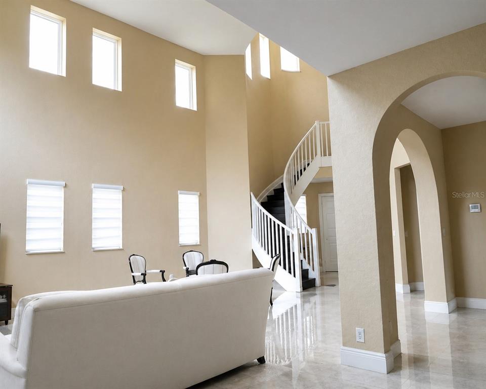 A living room with high ceilings, a curved staircase, and light-colored tile flooring — 143 NW 117TH AVENUE, PLANTATION, FL