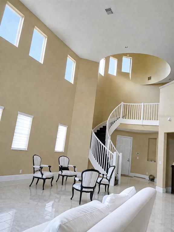A high-ceilinged living room features a curved staircase, light-colored tile floors, and several windows — 143 NW 117TH AVENUE, PLANTATION, FL