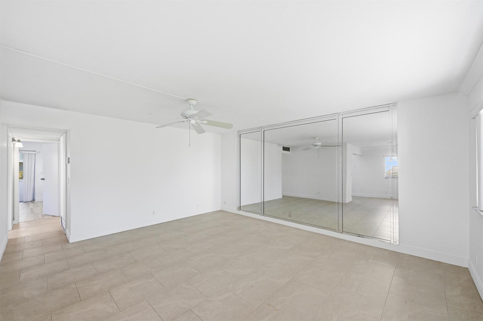 A bright room features white walls, light tile flooring, a ceiling fan, and mirrored closets — 452 Brittany J, Delray Beach FL 33446, DELRAY BEACH, FL