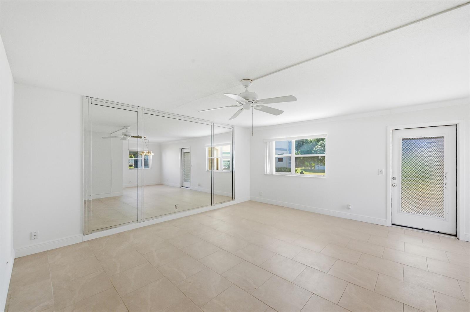 A bright, empty room features white walls, tiled floors, a ceiling fan, and mirrored walls — 452 Brittany J, Delray Beach FL 33446, DELRAY BEACH, FL