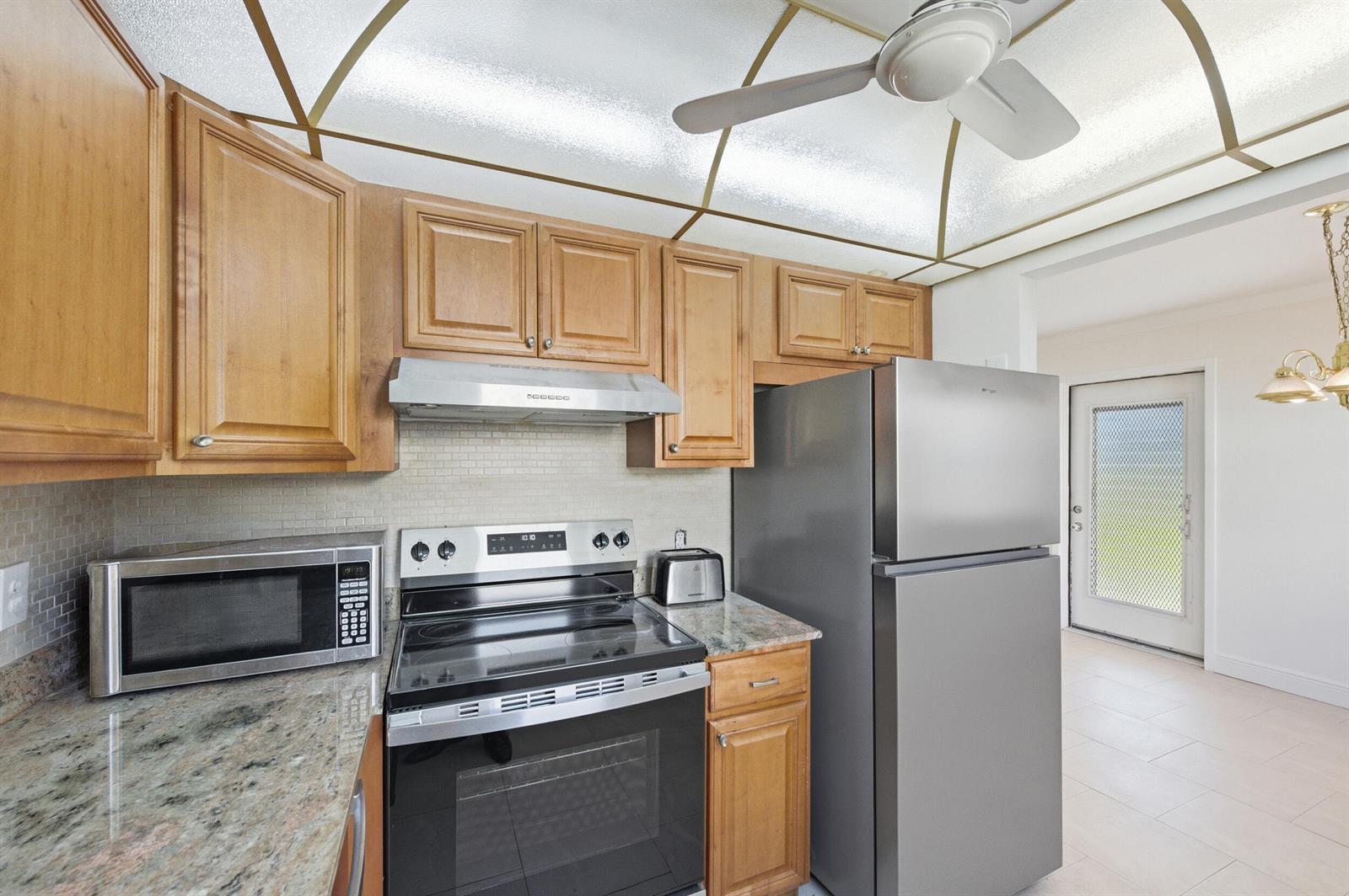 A kitchen features wood cabinets, stainless steel appliances, granite countertops, and a ceiling fan — 452 Brittany J, Delray Beach FL 33446, DELRAY BEACH, FL