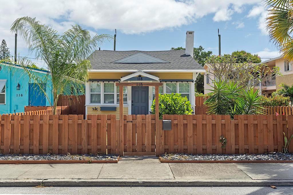 A yellow house with a wooden fence and a front gate stands under a blue sky — 118 S J Street, FL 33460, FL