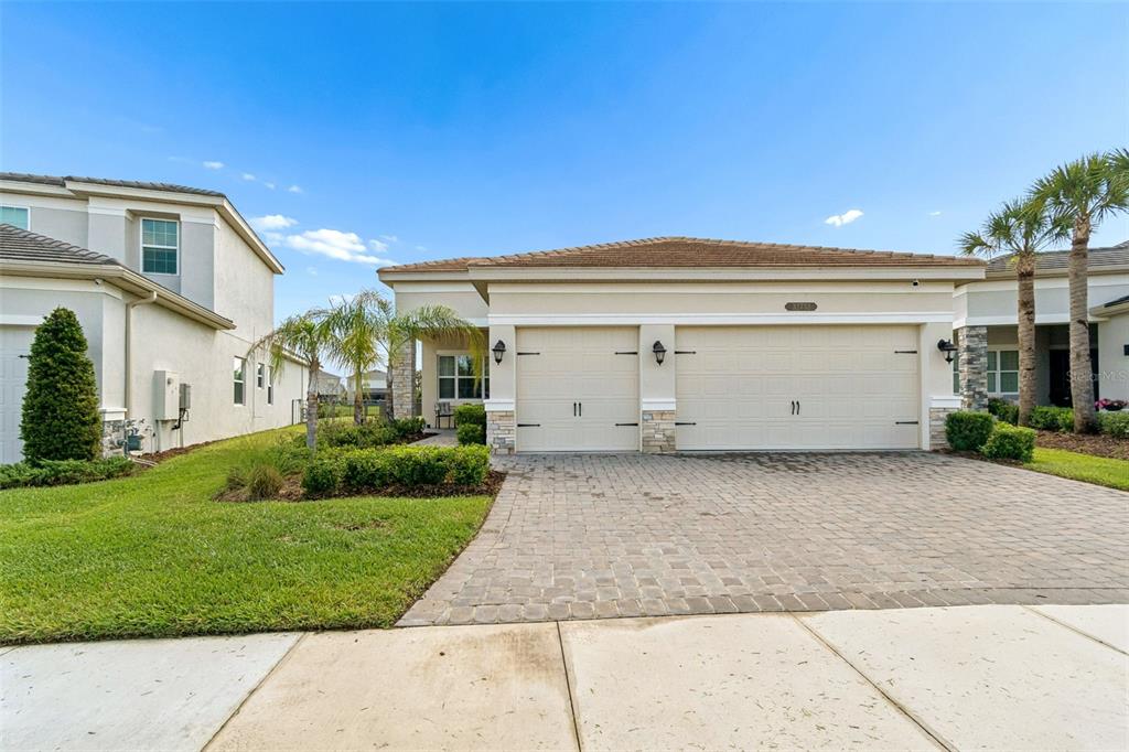A single-story house with a two-car garage and a paved driveway under a blue sky — 32732 TREE OF LIFE AVENUE, WESLEY CHAPEL, FL