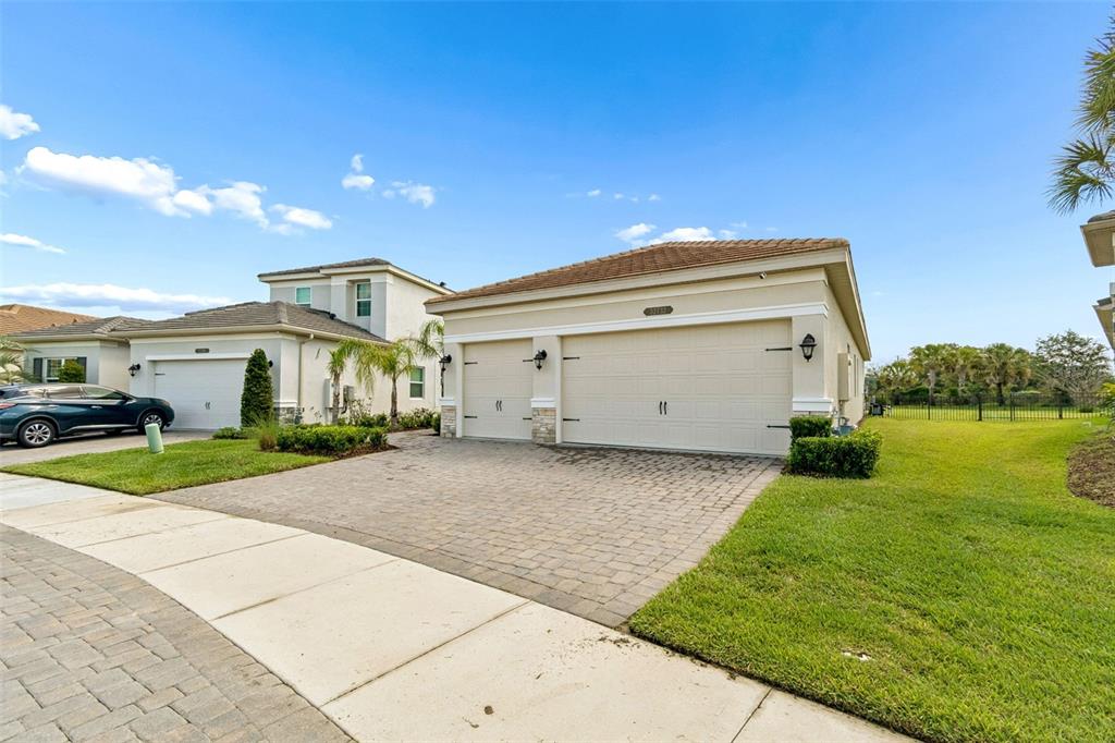 A beige single-story house with a three-car garage and a paved driveway — 32732 TREE OF LIFE AVENUE, WESLEY CHAPEL, FL