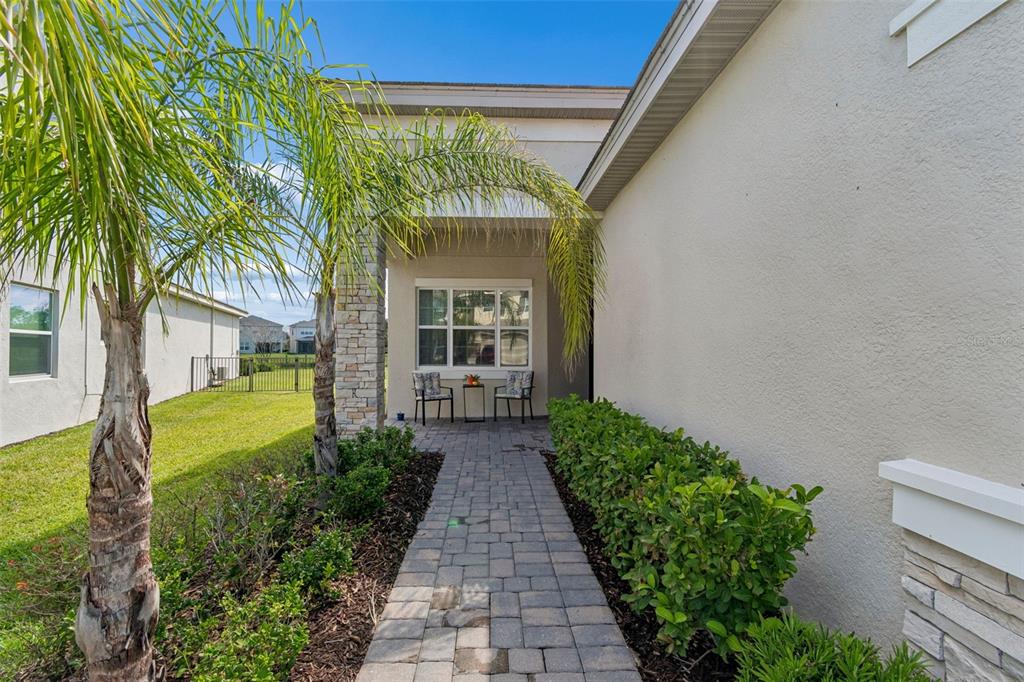 A stone-paved walkway leads to a covered entryway with two chairs and a palm tree — 32732 TREE OF LIFE AVENUE, WESLEY CHAPEL, FL