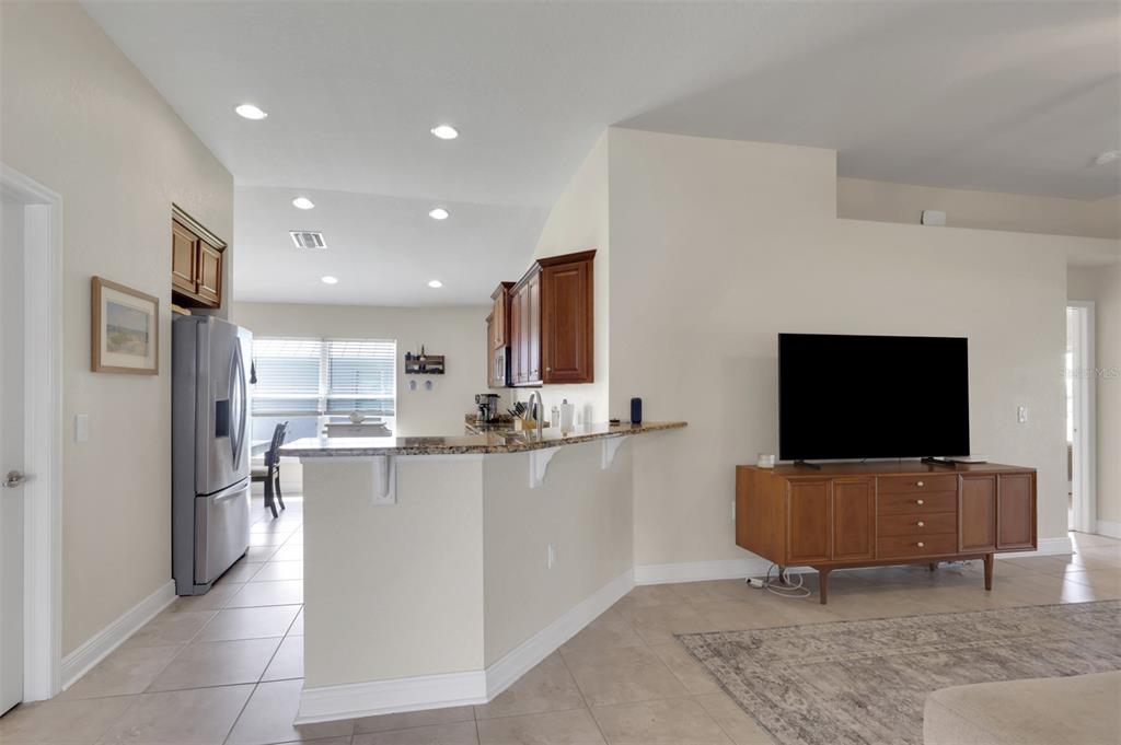 A kitchen with wood cabinets and granite countertops overlooks a living area with a television — 27077 BROOK FOREST ROAD, PUNTA GORDA, FL