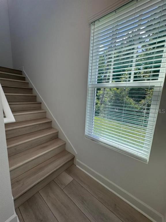 A staircase with light wood-look steps and flooring sits beside a window with white blinds — 7573 ESTUARY LAKE LOOP UNIT B, CELEBRATION, FL