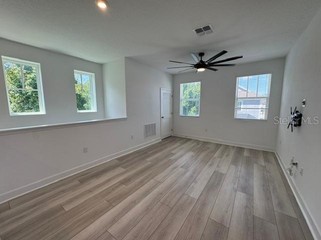 A bright, empty room features light wood-look flooring, white walls, and a ceiling fan — 7573 ESTUARY LAKE LOOP UNIT B, CELEBRATION, FL