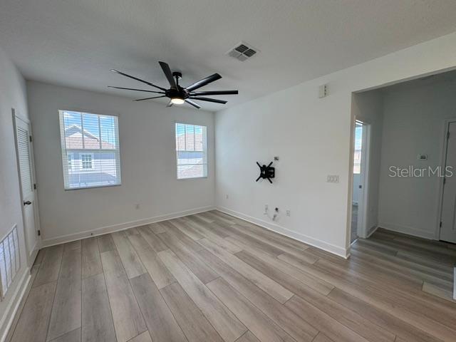 An empty room features light wood-look flooring, white walls, two windows, and a ceiling fan — 7573 ESTUARY LAKE LOOP UNIT B, CELEBRATION, FL