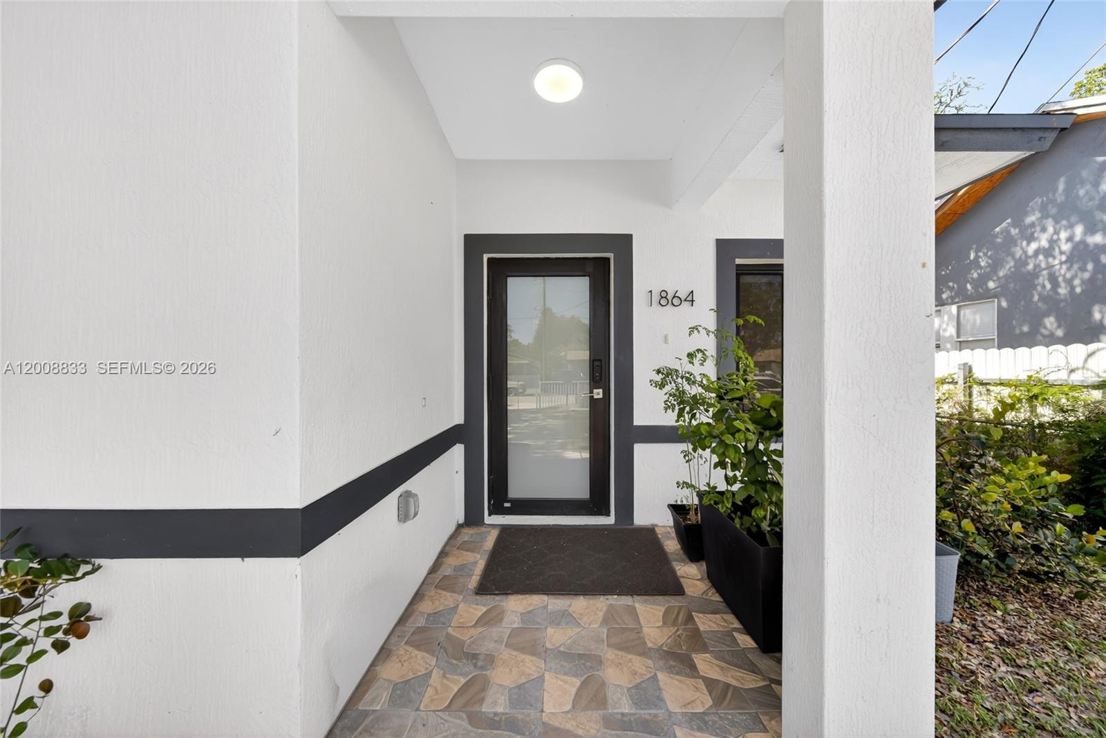 A covered entryway features a glass-paneled door, tiled flooring, and a potted plant — 1864 NW 84th St, Miami FL 33147, MIAMI, FL