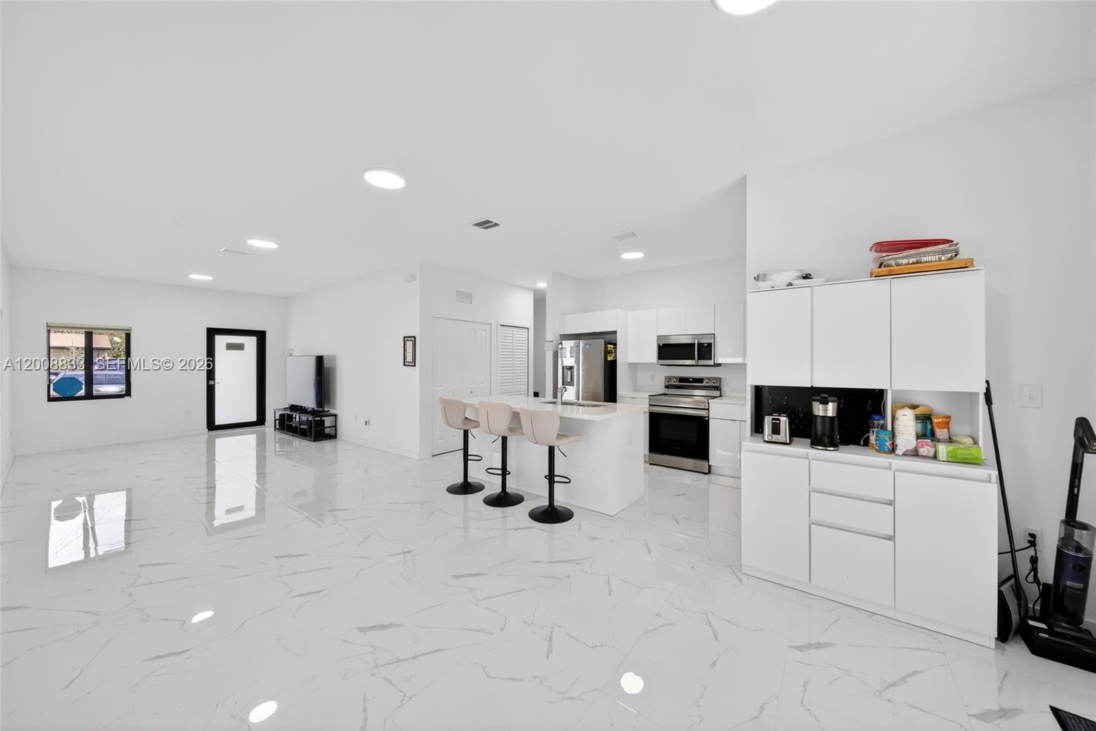 A bright, open-concept kitchen and living area features white cabinetry, marble-patterned tile floors, and an island — 1864 NW 84th St, Miami FL 33147, MIAMI, FL