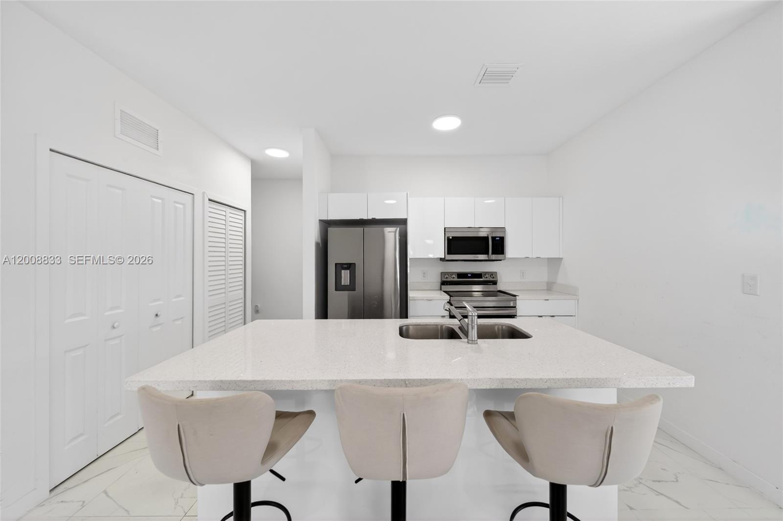 A modern kitchen features white cabinetry, stainless steel appliances, and a central quartz island — 1864 NW 84th St, Miami FL 33147, MIAMI, FL