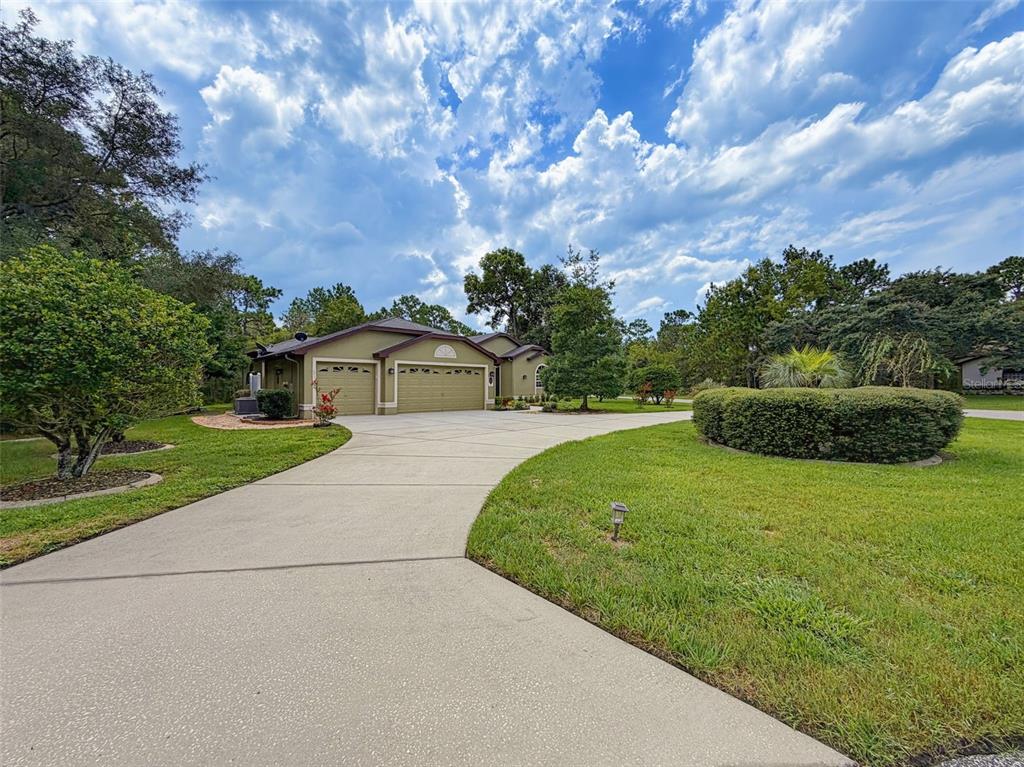 A wide concrete driveway leads to a single-story house with a three-car garage — 1 PLUMBAGO DRIVE, HOMOSASSA, FL