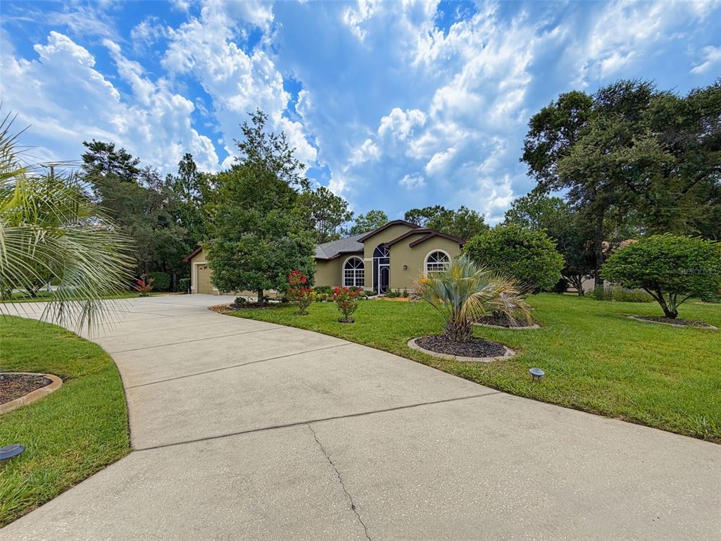 A single-story house with a concrete driveway, green lawn, and trees under a cloudy sky — 1 PLUMBAGO DRIVE, HOMOSASSA, FL