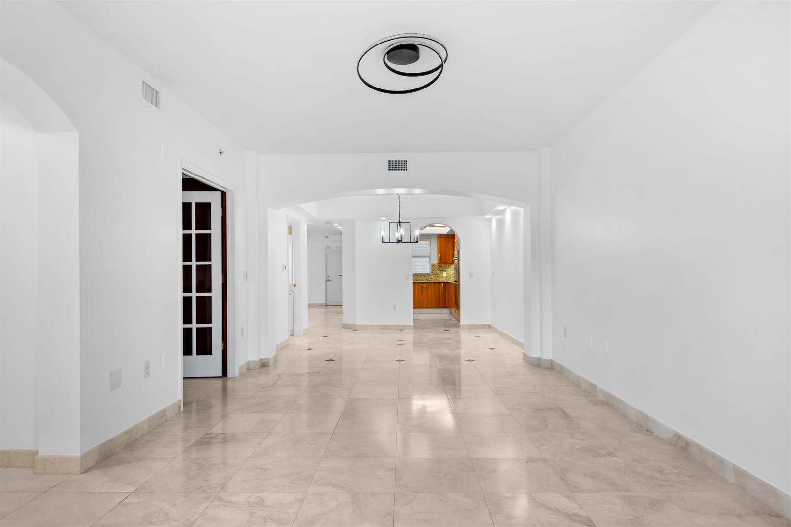 An empty room with light-colored tile flooring, white walls, and an arched entryway to a kitchen — 2051 SE 3rd Street, Deerfield Beach FL 33441, DEERFIELD BEACH, FL
