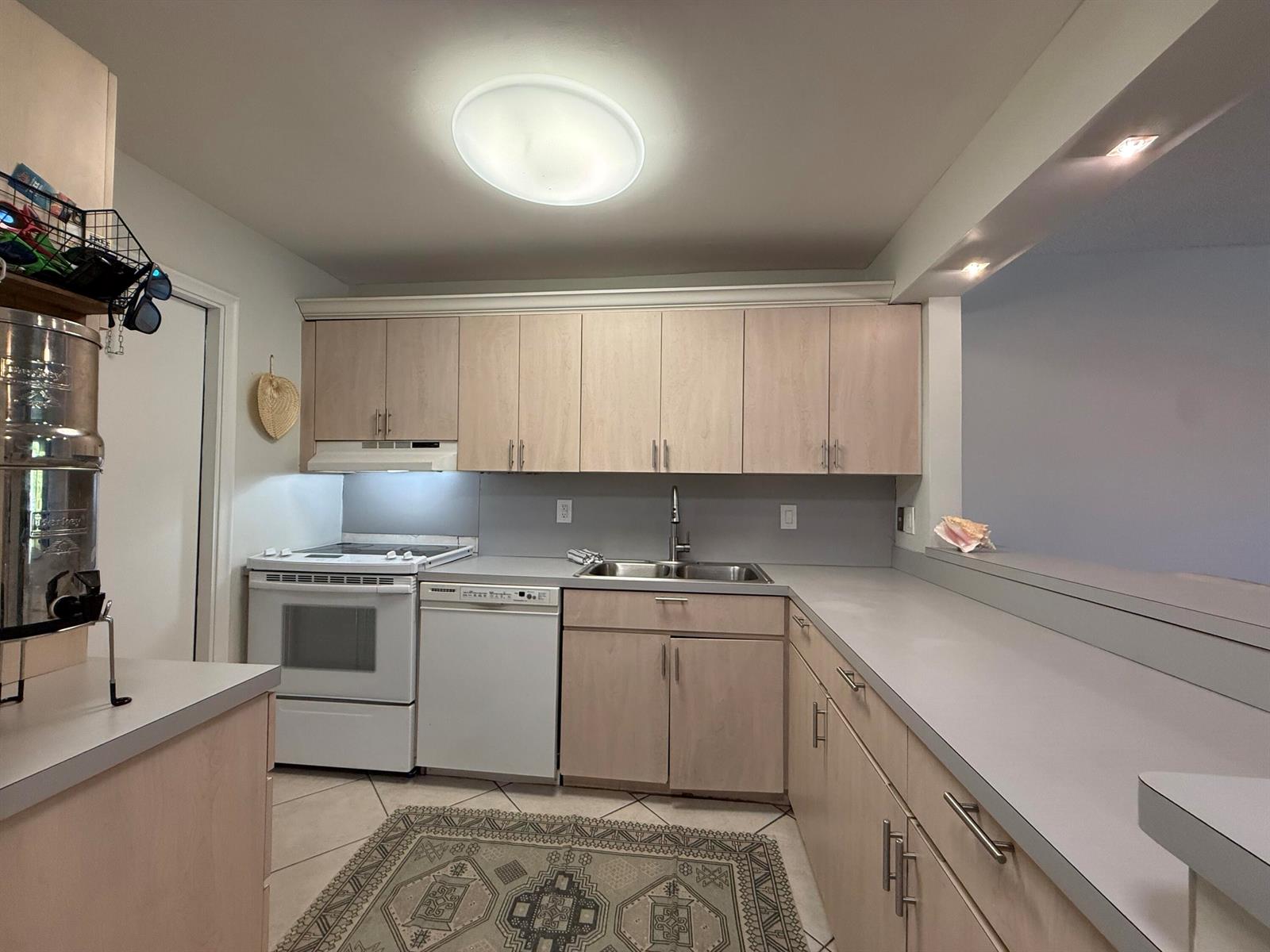A kitchen features light wood cabinets, white appliances, gray countertops, and a patterned area rug — 1040 SE 4th Avenue # 331, Deerfield Beach FL 33441, DEERFIELD BEACH, FL