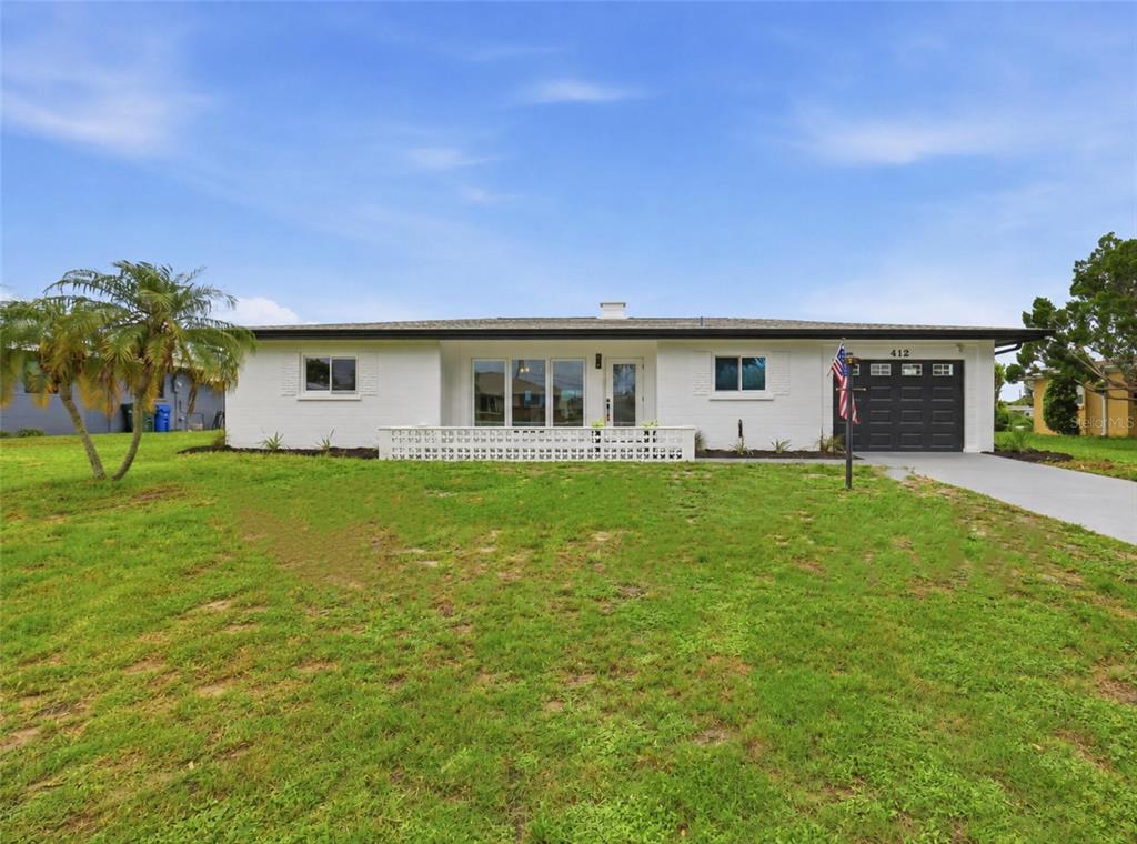 A single-story white brick house features a dark garage door and a front lawn — 412 W SHADE DRIVE, VENICE, FL