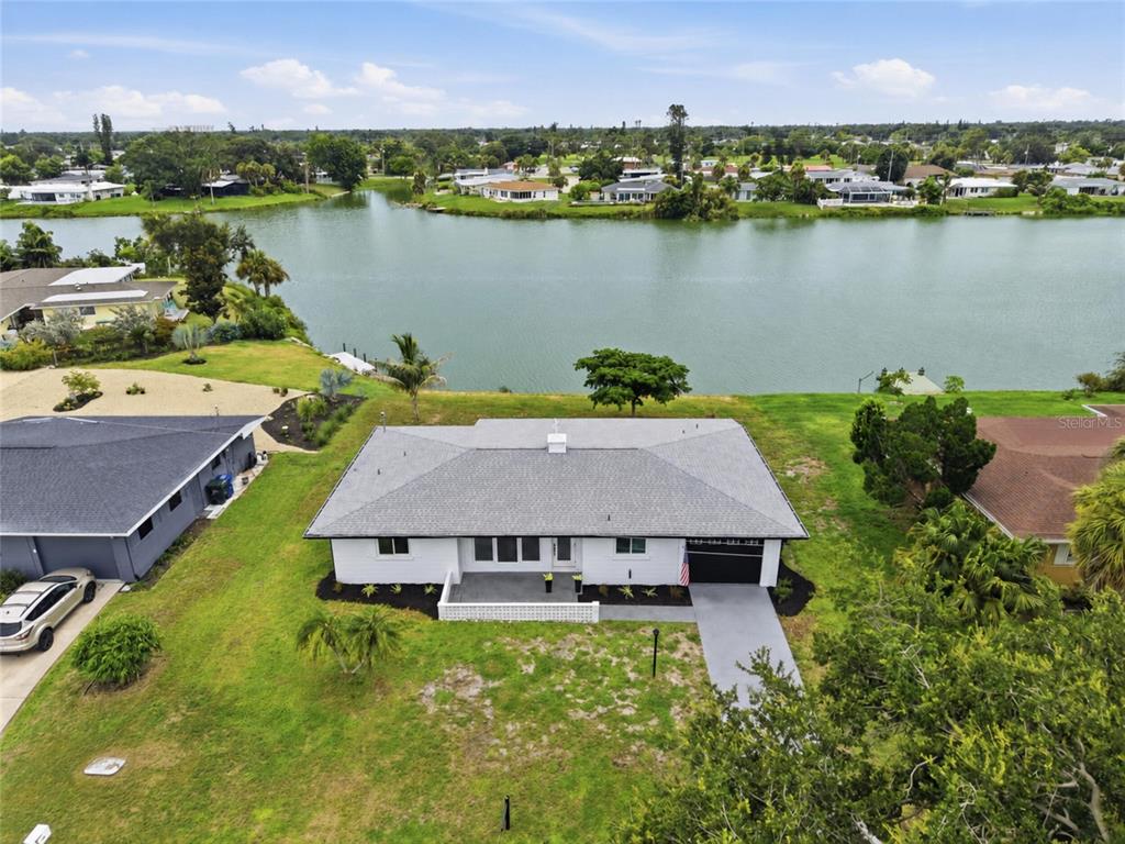An aerial view shows a white single-story house with a gray roof overlooking a lake — 412 W SHADE DRIVE, VENICE, FL
