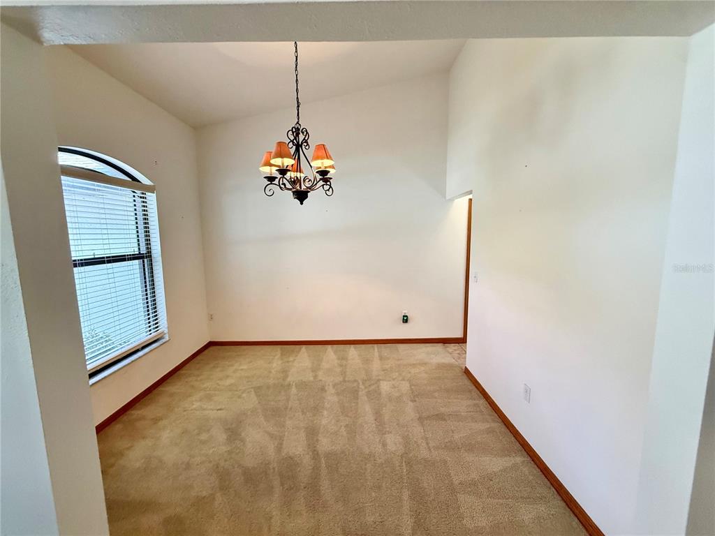 An empty dining room features beige carpeting, a vaulted ceiling, and a hanging chandelier — 4843 CALASANS AVENUE, ST CLOUD, FL
