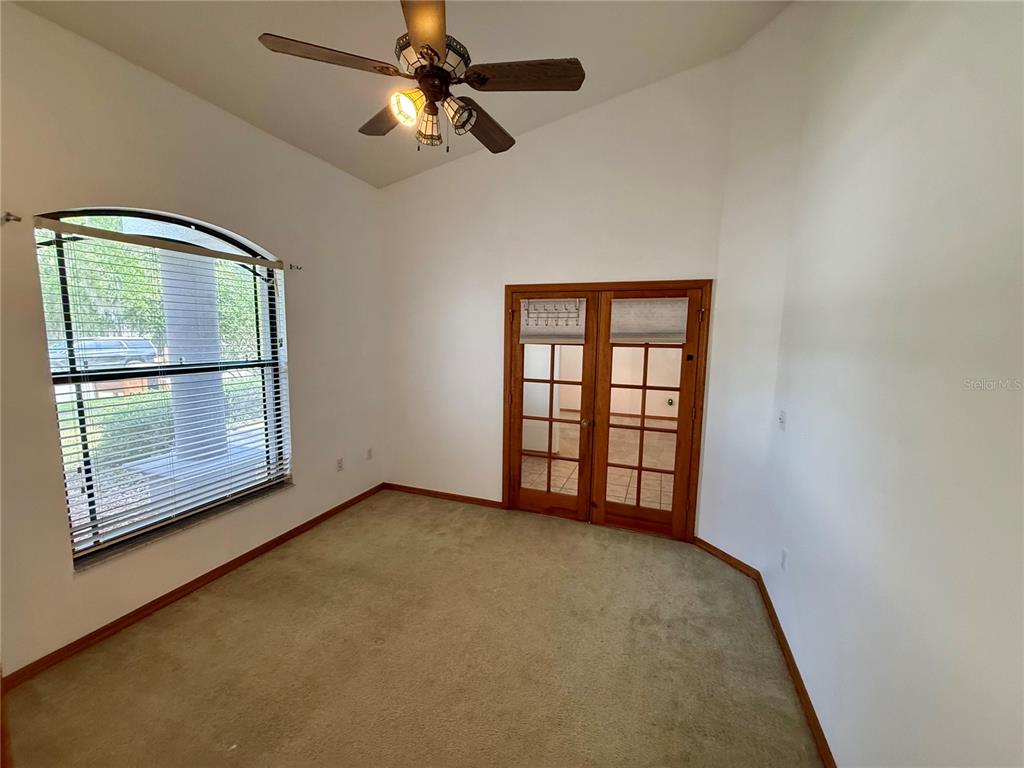 An empty room features beige carpet, a ceiling fan, an arched window, and French doors — 4843 CALASANS AVENUE, ST CLOUD, FL